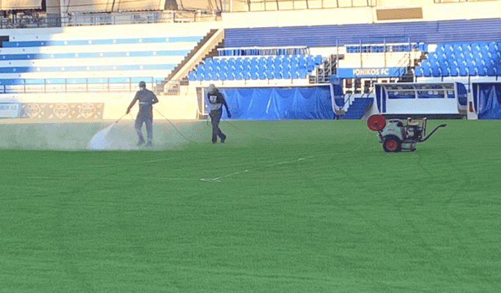 Two workers maintaining a football field by spraying the grass.
